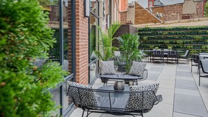 Ein Patio im Freien mit schwarzer Rattanmöbeln, Topfpflanzen und einer Ziegelwand.