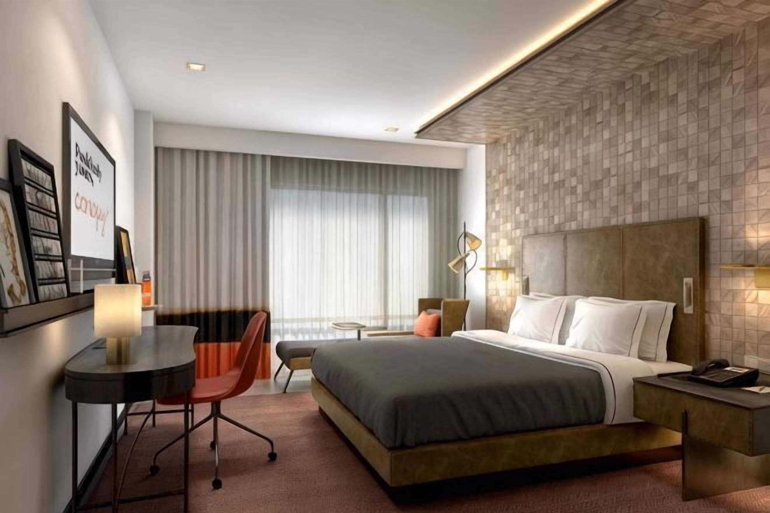 Hotellihuone, jossa on sänky, työpöytä, tuoli ja suuri ikkuna, jossa on verhot.