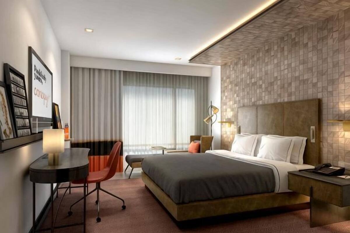 A hotel room with a bed, desk, chair, and a large window with curtains.