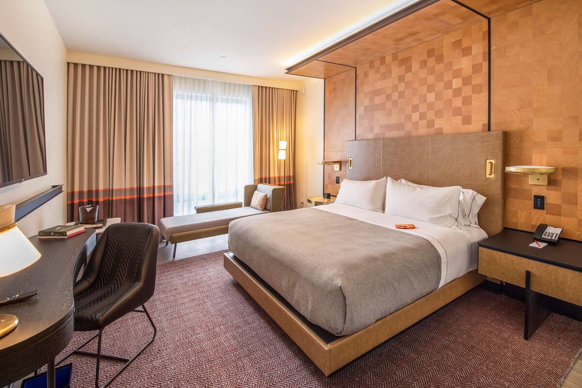 A hotel room with a large bed, a desk with a chair, a TV, and a window with curtains.