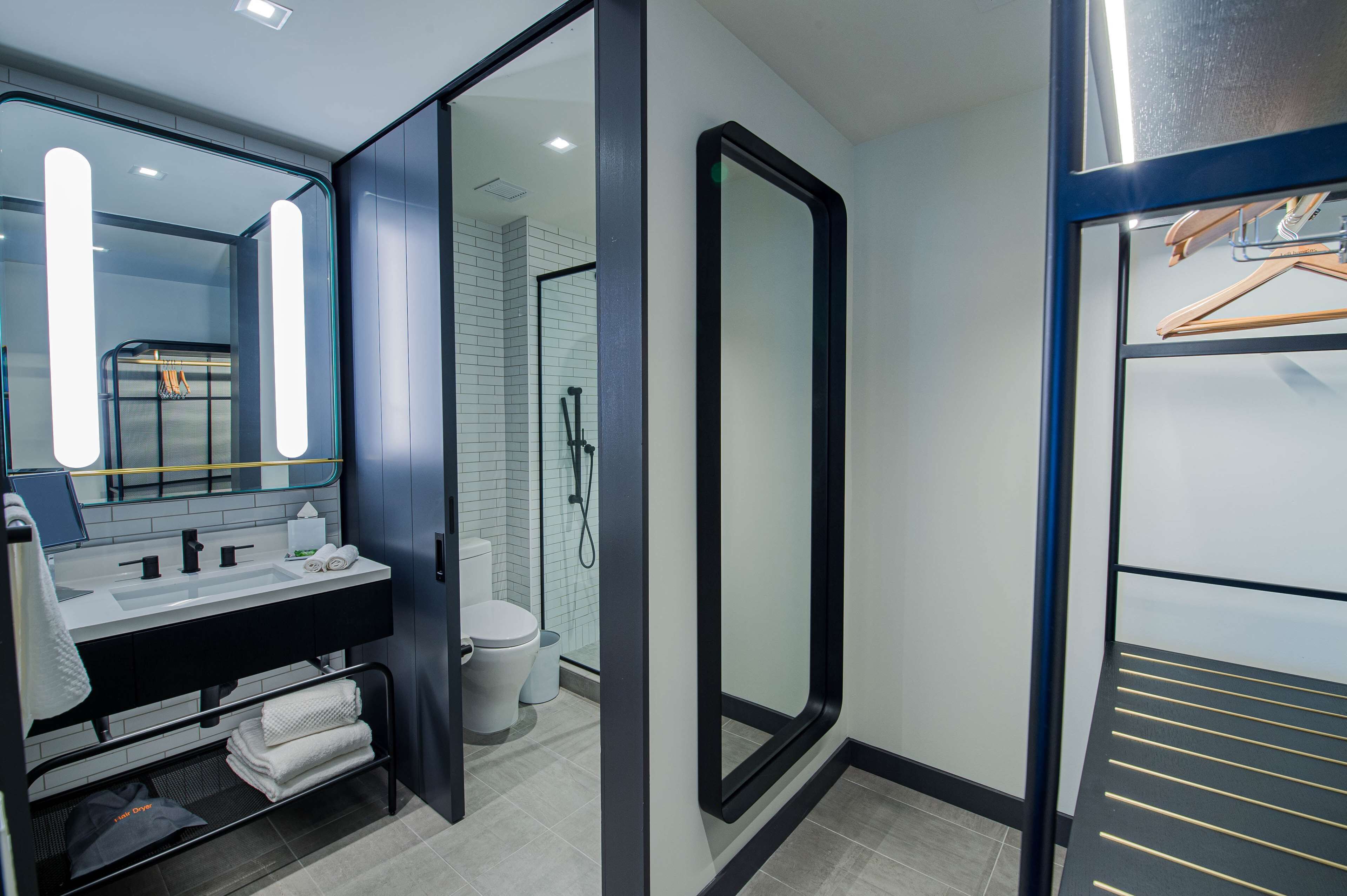 Un baño moderno con tocador de doble lavabo, cabina de ducha con paredes de vidrio y vestidor con estante metálico.