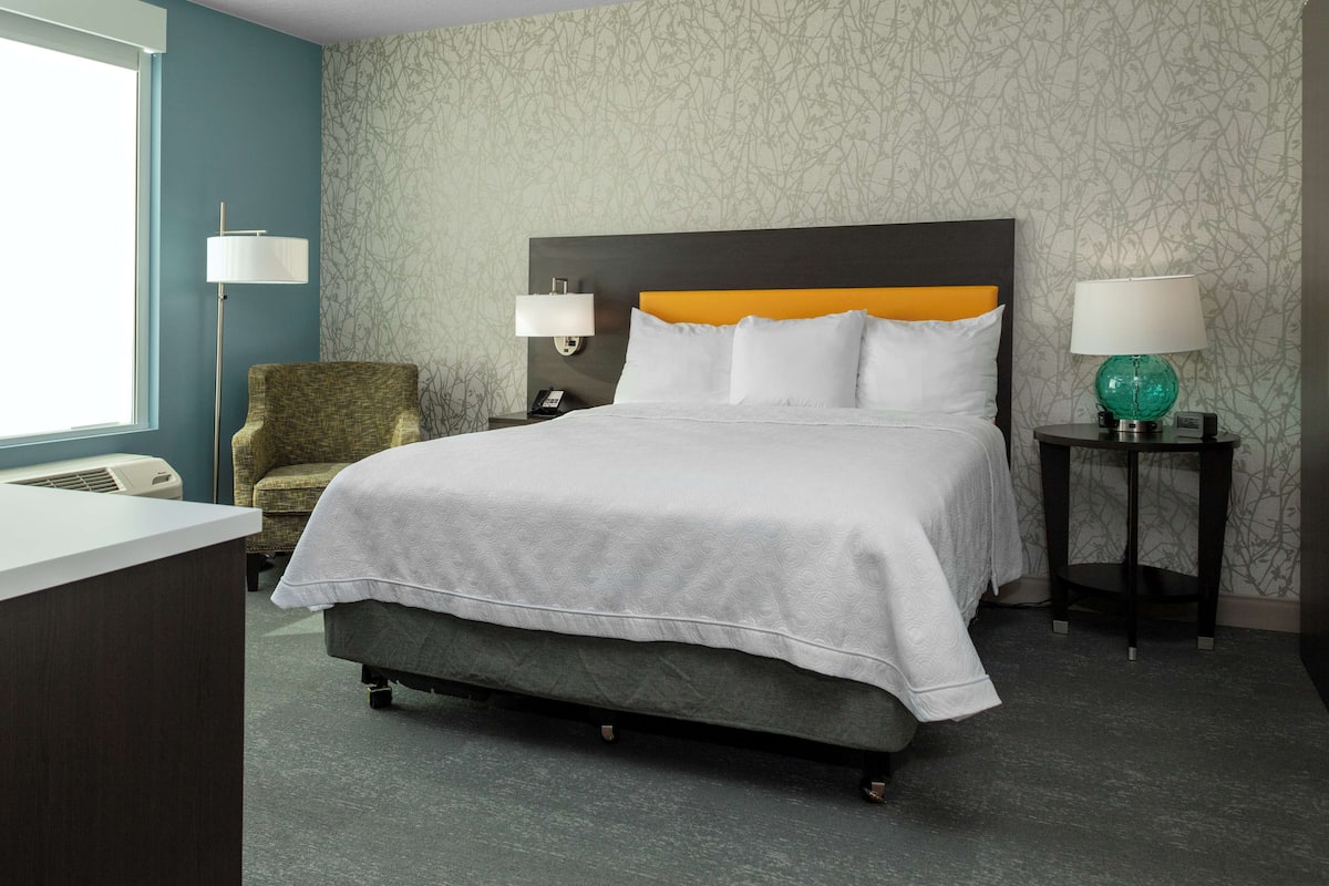 Una habitación de hotel con una cama, dos lámparas de noche, una silla y un escritorio.