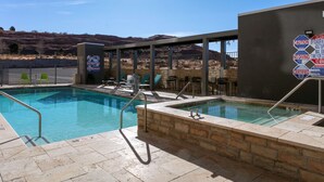 A pool area with two separate pools, a covered seating area, and a view of hills in the background. - Home2 Suites by Hilton Page Lake Powell (Page)