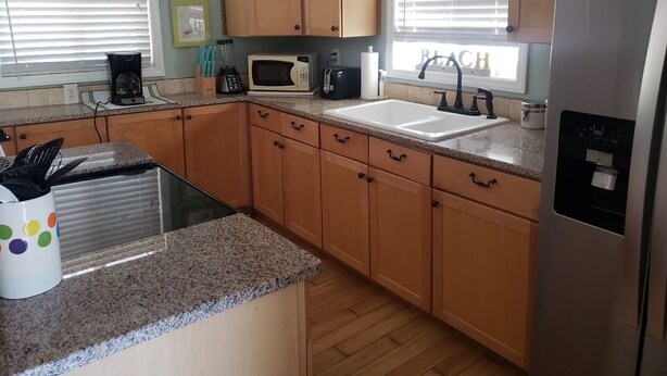 A kitchen with wooden cabinets, a granite countertop, a stainless steel refrigerator, a microwave, a toaster, and a coffee maker.