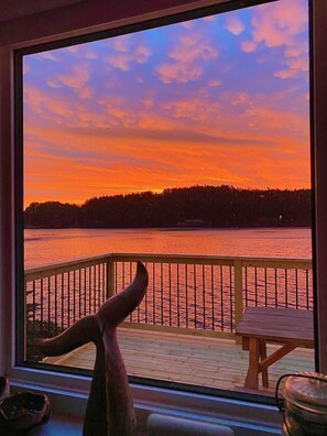 Vista dalla finestra su un tramonto sul lago, con un molo e un pontile in legno.