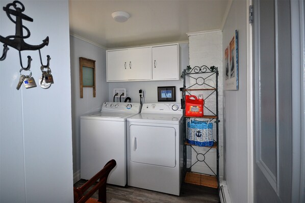 A laundry room with two white front-loading washing machines, a drying rack, and a small cabinet above. - Salt harbor cottage (Salt Harbour Herring Neck)