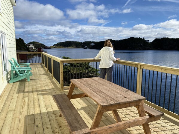Un pontile in legno con tavolo e sedie da picnic, affacciato su una distesa d'acqua tranquilla e colline sullo sfondo.