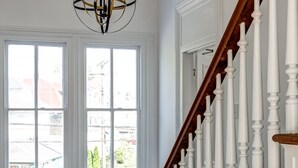 A staircase with white balusters and a wooden handrail leading to a landing with a hanging light fixture. - The Ashley Rose (Cape May)