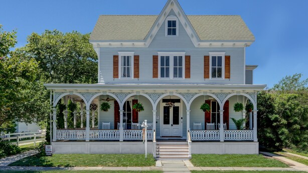 A two-story house with a porch, white siding, and a gabled roof. - The Ashley Rose (Cape May)