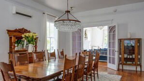 A dining room with a large wooden table, chairs, a chandelier, and a cabinet with dishes. - The Ashley Rose (Cape May)