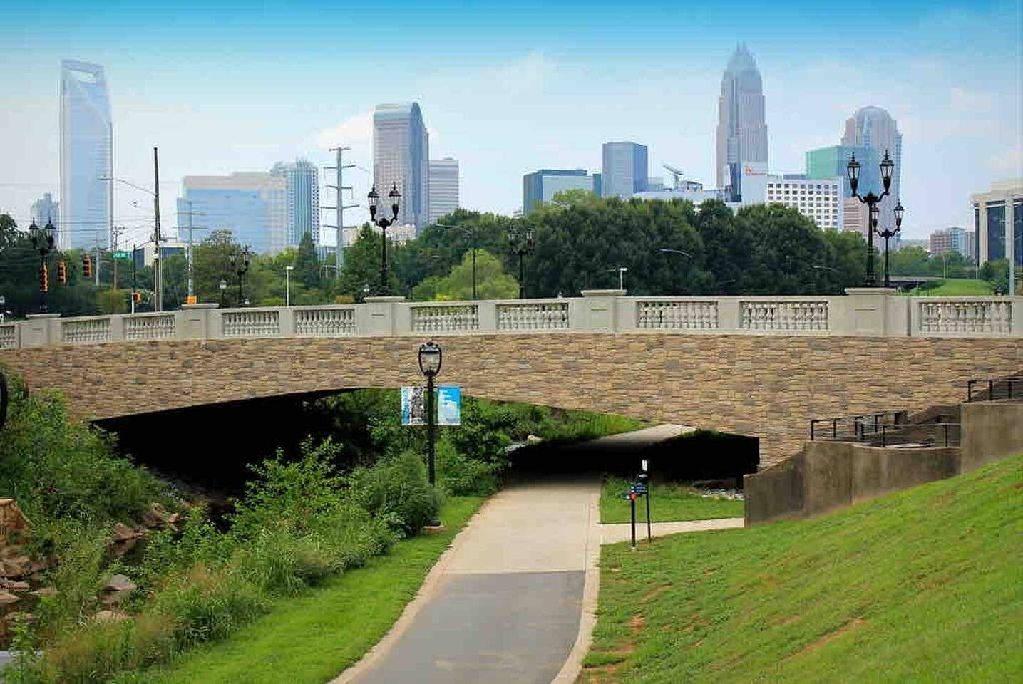 A cityscape with a stone bridge, a pedestrian path, and a grassy area.