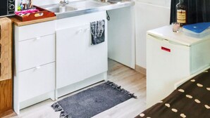 Eine kleine Küche mit weißen Schränken, einem Spülbecken, einer Arbeitsplatte und einem Fenster mit Vorhängen.
