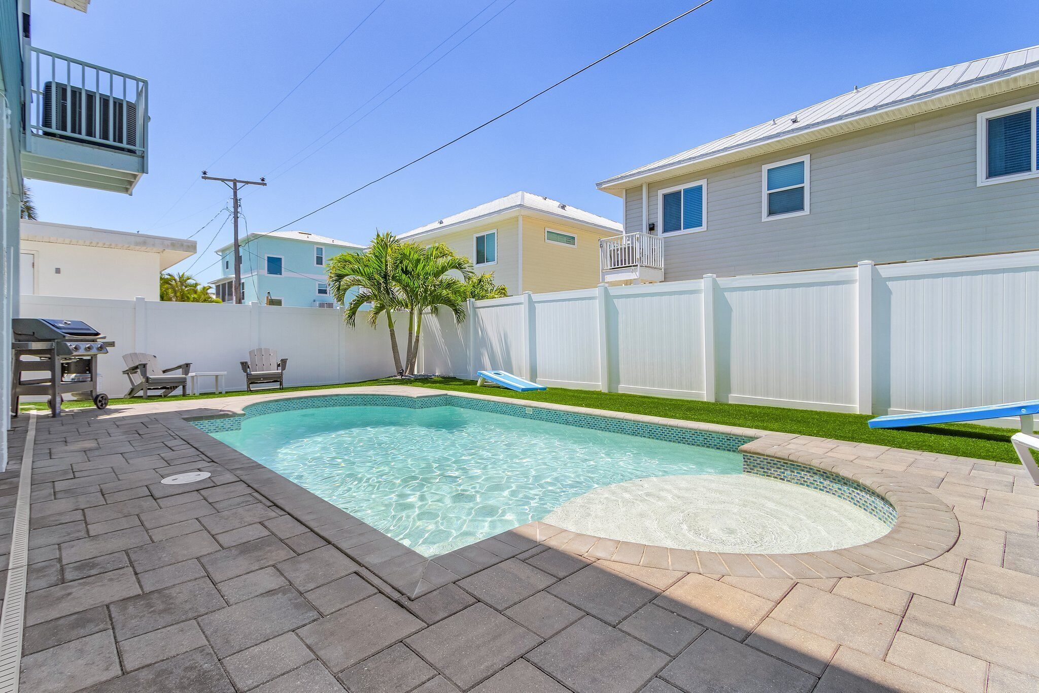 Um quintal com piscina, um alpendre com cadeiras e um muro branco.