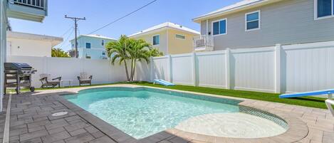 Um quintal com piscina, um alpendre com cadeiras e um muro branco.