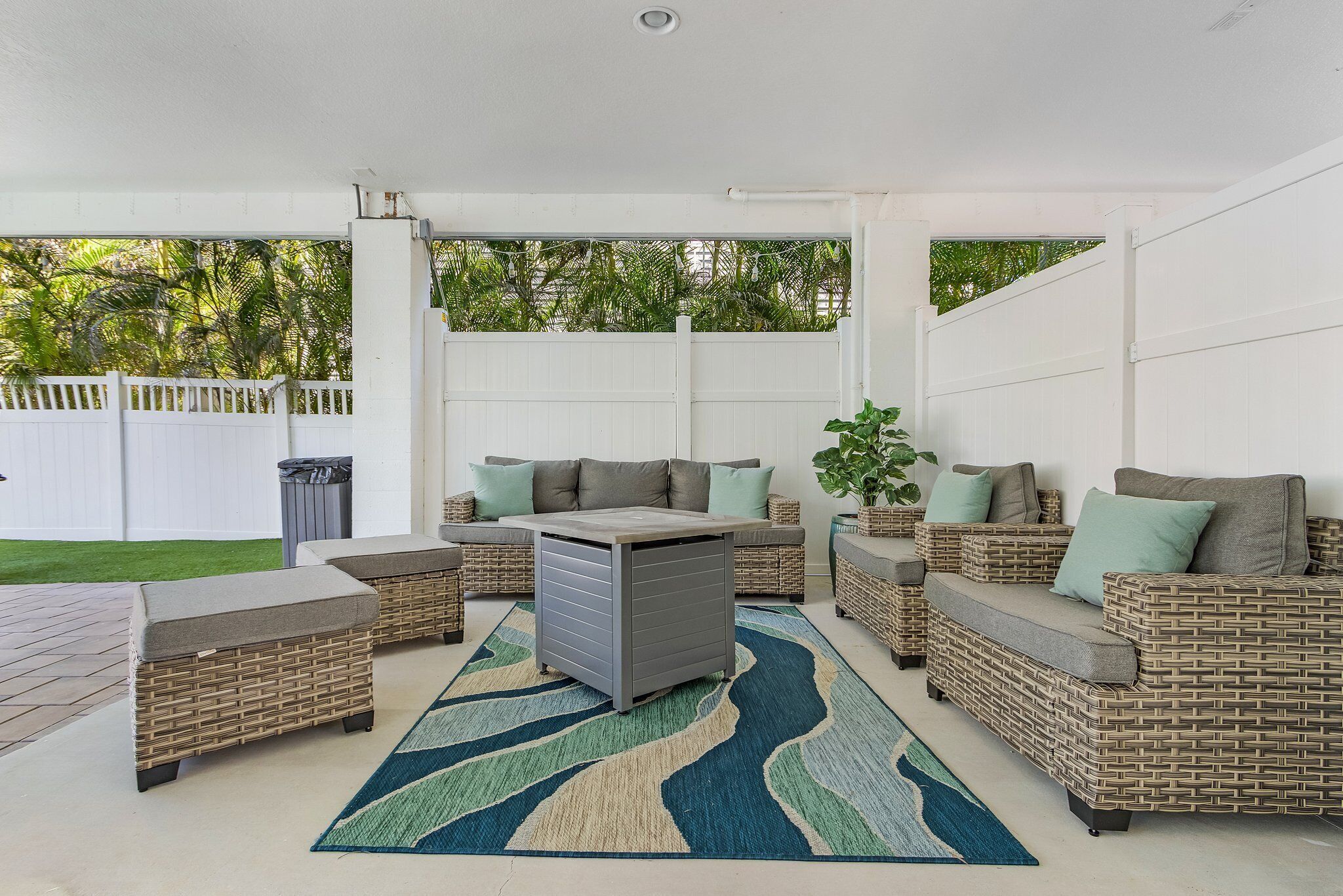 Un patio al aire libre con mobiliario de mimbre, un mueble de almacenamiento gris y un tapete estampado.