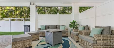 Un patio al aire libre con mobiliario de mimbre, un mueble de almacenamiento gris y un tapete estampado.