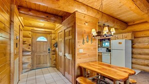 A log cabin interior with a wooden dining table, bench, kitchen area, and a door leading to another room. - Star Views - 2BR/New Hot Tub/New Firepit/Grill/Sleeps 8 (Gatlinburg)