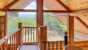 A wooden cabin with a balcony, large windows, and a view of a forested mountain range. - Star Views - 2BR/New Hot Tub/New Firepit/Grill/Sleeps 8 (Gatlinburg)