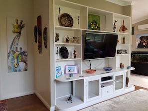 A living room with a white entertainment unit, a flat-screen TV, and various decorative items. - Relax and Enjoy a little bit of Sanctuary in Jervis Bay (Sanctuary Point)