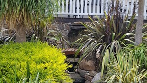 Ein Garten mit vielfältigen Pflanzen, einem kleinen Bach und einem weißen Zaun.
