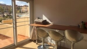 A balcony with a glass door, a wooden table, and three bar stools.