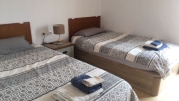 A room with two beds, each with patterned bedding and a wooden headboard. There is a nightstand with a lamp between the beds.