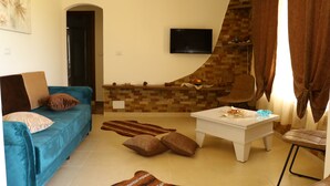 Una sala de estar con un sofá azul, una mesa de centro blanca, un televisor de pantalla plana y piso de baldosas.