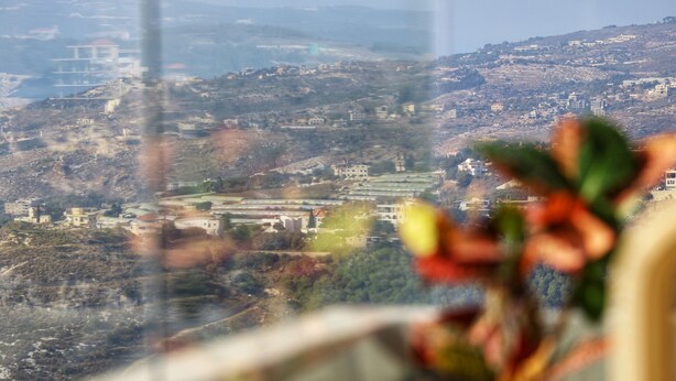 Vista desde una ventana que da a un paisaje montañoso con edificios y vegetación.