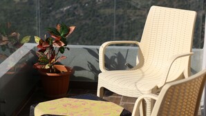 Una silla de mimbre y una planta en maceta en un balcón con vistas a un paisaje montañoso.