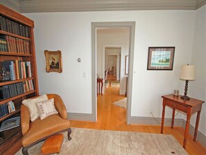 A living room with a leather armchair, a wooden bookshelf, a framed picture, and a lamp on a side table.