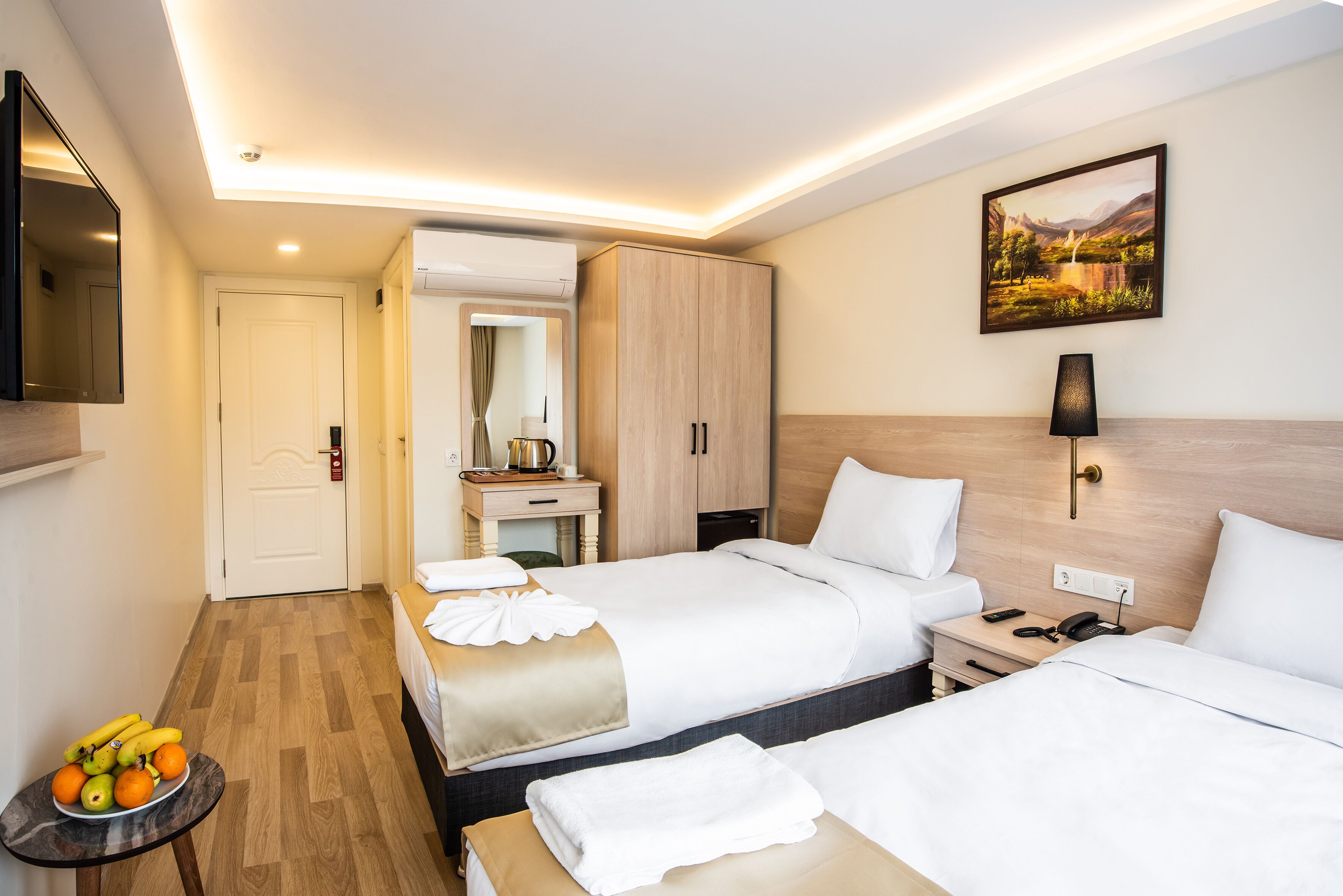 A hotel room with two beds, a desk, a mirror, and a painting on the wall.