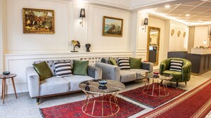 Una sala moderna con un sofá gris, un sillón verde y una alfombra roja con estampado. Hay dos mesitas con tapas de mármol negro y patas doradas.