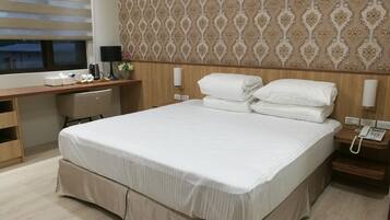 Habitación de hotel con una cama grande, un escritorio, una silla, una mesita de noche con teléfono y una pared con papel tapiz estampado.