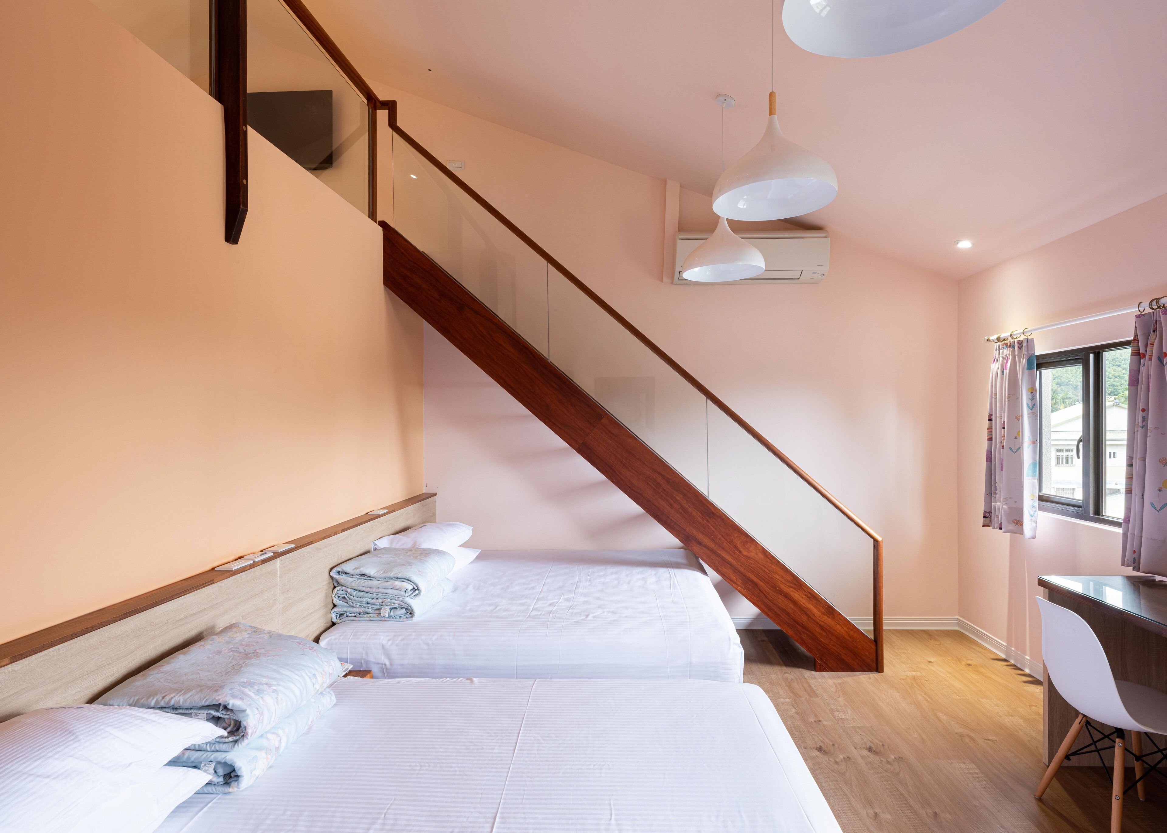 A bedroom with two beds, a wooden staircase, a desk, and a window with curtains.