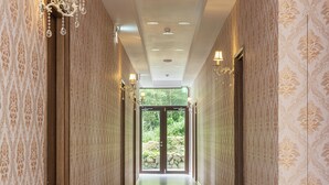 A hallway with patterned wallpaper, recessed lighting, and a view of greenery outside. - Minzu Hotel (Lugu)