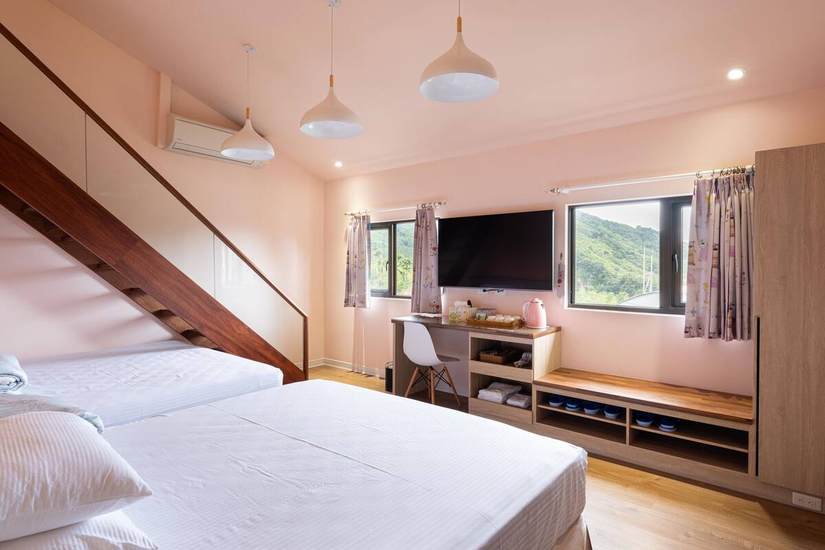 A bedroom with a bed, a desk, a TV, and a window with curtains.