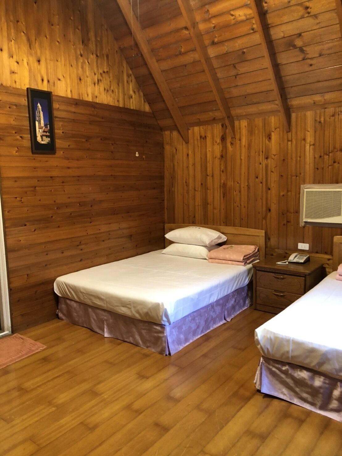 Un dormitorio de cabaña de madera con dos camas, una mesita de noche con un teléfono y un cuadro en la pared.