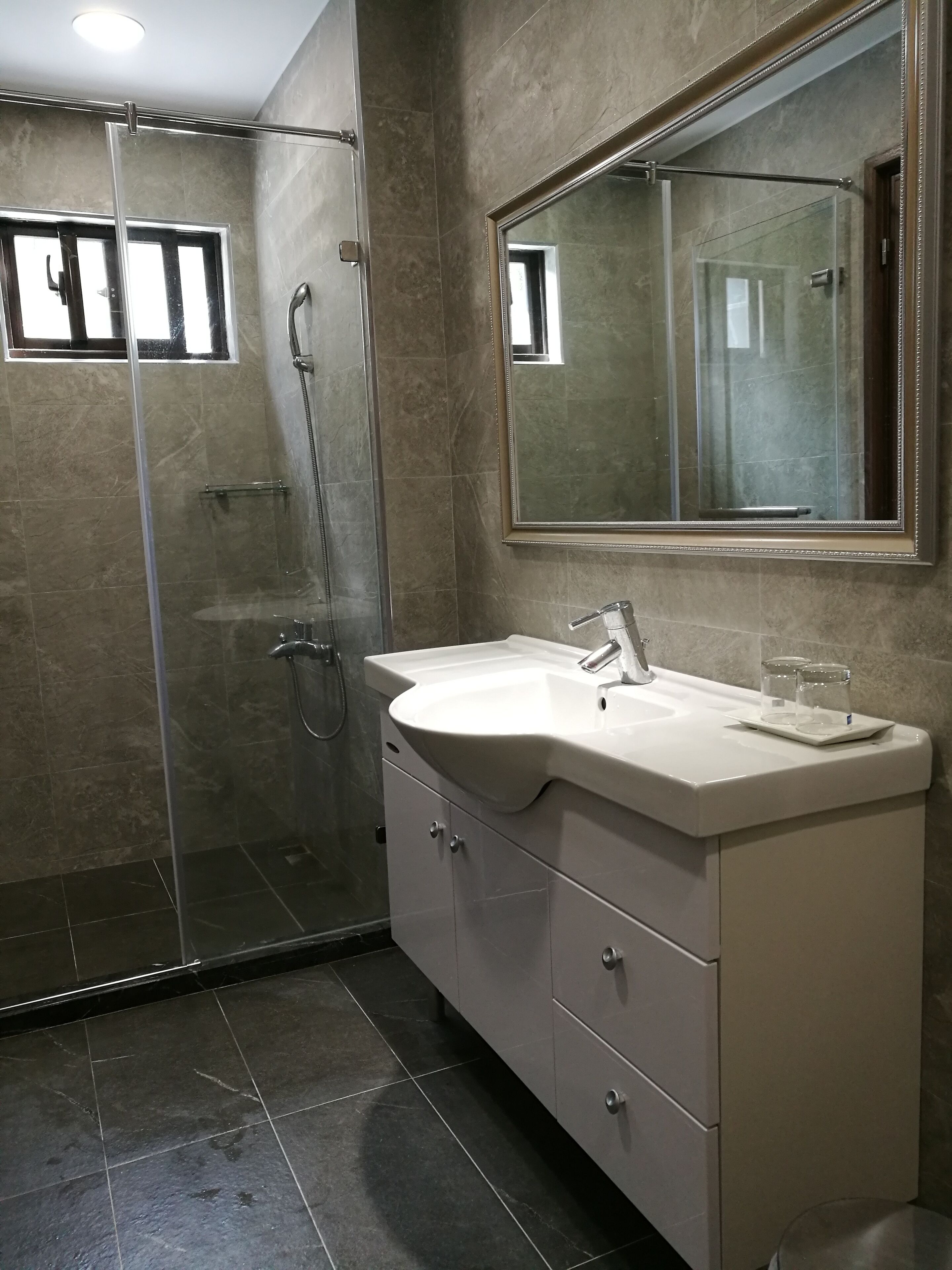 A modern bathroom with a glass shower enclosure, a white sink with a mirror above it, and a vanity with drawers.