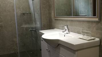 Une salle de bain moderne avec une douche à parois de verre, un lavabo blanc avec un miroir au-dessus et un meuble-lavabo avec des tiroirs.