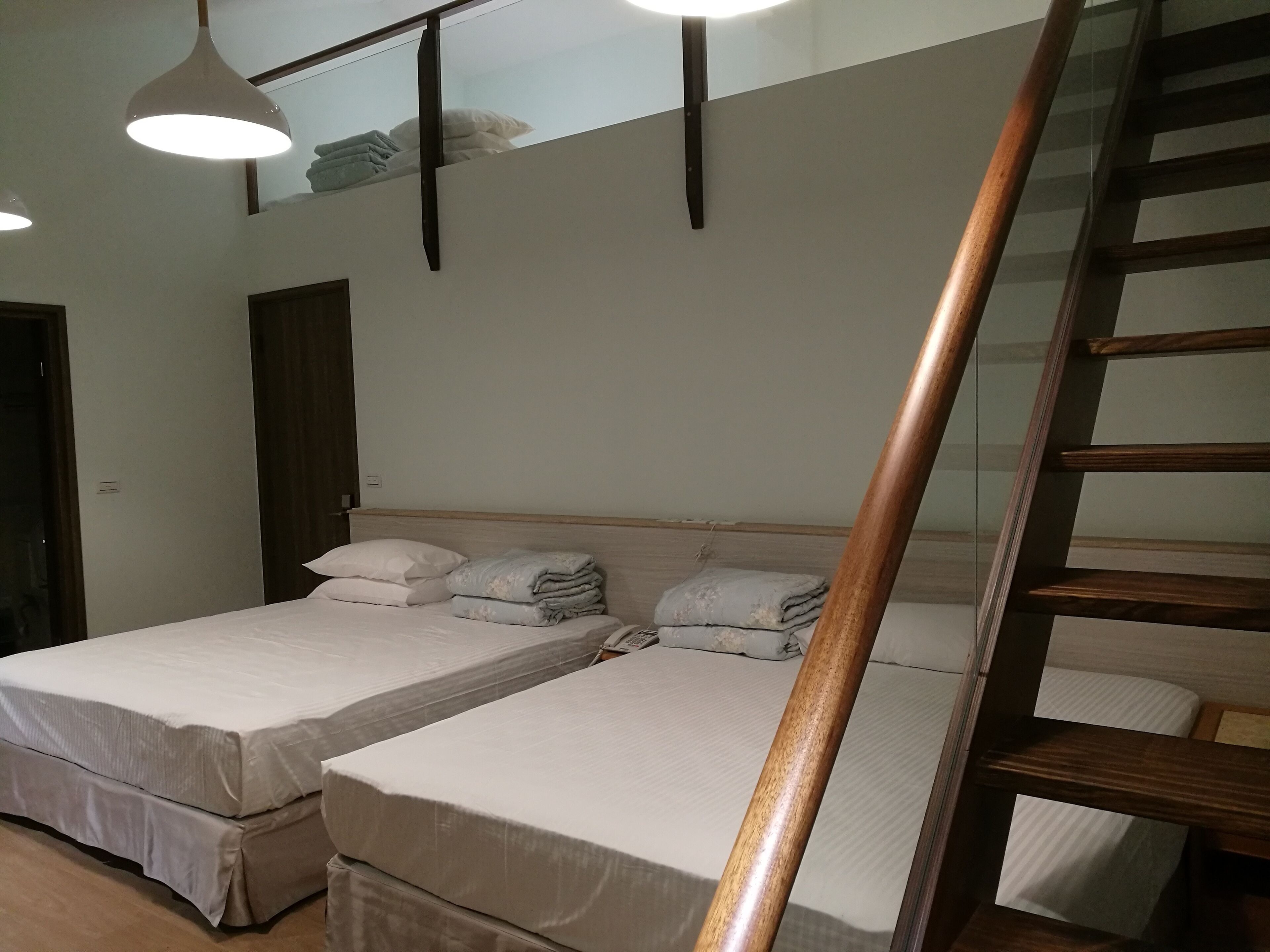 A hotel room with two beds, a wooden staircase, and a ceiling light fixture.