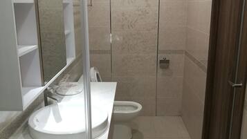 Une salle de bain avec un lavabo blanc, un miroir, des toilettes et un espace douche.