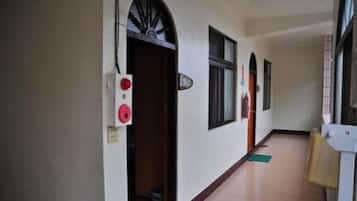 A hallway with a door leading to a room, a fire alarm, and a window.