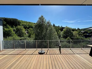 Un terrazza in legno con ringhiera metallica, affacciata su un pendio boscoso.