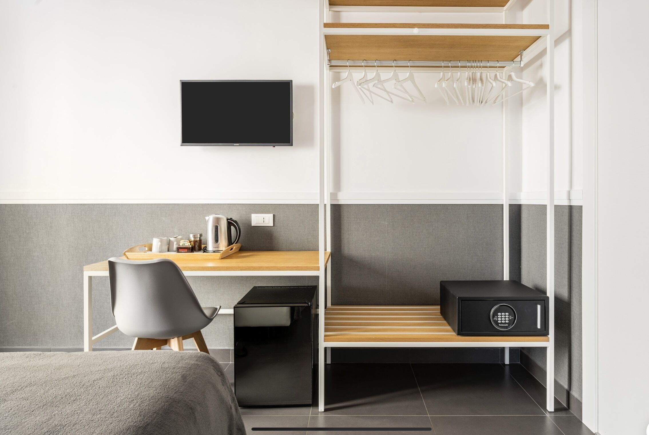 Une chambre d’hôtel de taille réduite, comprenant un lit, un bureau avec une chaise, une télévision et un coffre-fort.