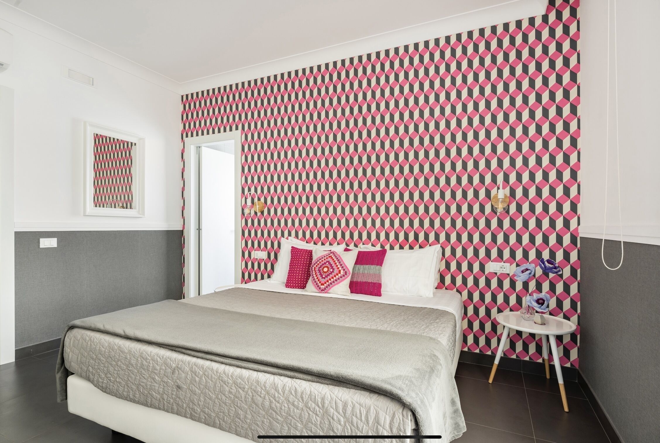 Een moderne slaapkamer met behang met een patroon, een bed met een gewatteerde hoes en een klein nachtkastje met schoenen.