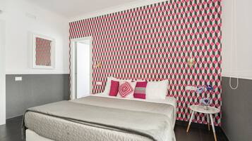 Een moderne slaapkamer met behang met een patroon, een bed met een gewatteerde hoes en een klein nachtkastje met schoenen.