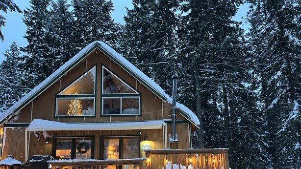 A cabin with a porch, large windows, and a chimney.
