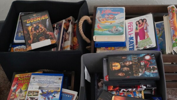 Una colección de DVD y libros en estanterías y un cesto negro para guardar objetos.
