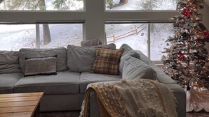 A cozy living room with a large window, a Christmas tree, and a clock on the wall.