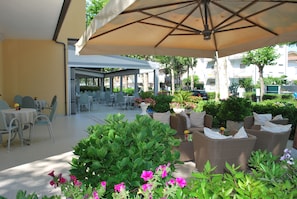 Un espace extérieur aménagé en terrasse, avec des tables et des chaises, entouré de verdure et de fleurs.